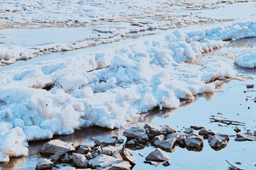 Spring ice drift on the river. Stones on the coast. Melting ice. Sunny evening.