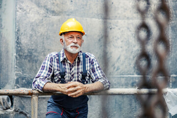 A senior heavy industry factory worker on his head leans on the railing in the facility and...