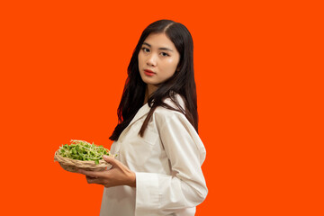 Vegetarian concept, Healthy woman hold basket of sunflower sprouts isolated over orange background
