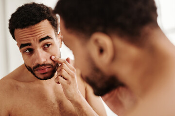 Young handsome man examining his face while looking at mirror in the morning