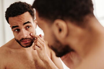 Young handsome man examining his face while looking at mirror in the morning