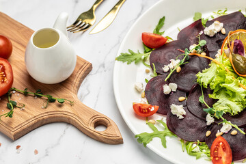 Beet or beetroot salad with greens, cheese, nuts, cranberries on plate with fork, dressing and spices on white background. italian cuisine. banner, menu, recipe place for text, top view