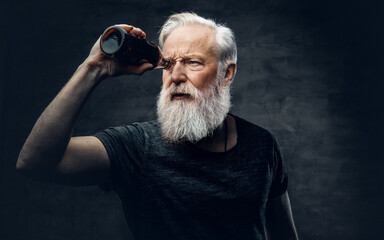 Portrait of muscular old man looking through bottle against dark background.