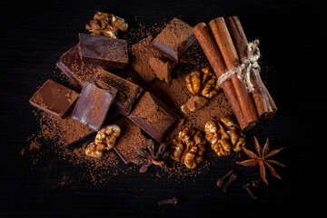 A pile of dark broken chocolate sprinkled with cocoa powder, nuts and spices. Copy space