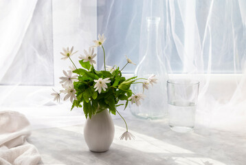 A beautiful bouquet of snowdrops in a glass vase near the window on the windowsill