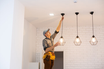 Electrician worker installation electric lamps light inside apartment. Construction decoration concept. - obrazy, fototapety, plakaty