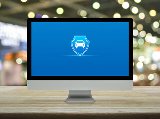 Car with shield flat icon on desktop modern computer monitor screen on wooden table over blur light and shadow of shopping mall, Business automobile insurance online concept