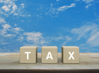 TAX letter on wood block cubes on wooden table over blue sky with white clouds, Business and finance concept