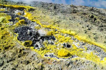 Yellow Sulphur on surface of rocks on top of a volcano crater on the island of Vulcano, Aeolian Archipelago. Sicily, Italy. Gray white and Yellow background of Sulfur. Steam and smoke from fumarole

