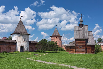Fototapeta na wymiar Yuryev-Polsky, Russia. Towers of fortified wall of Archangel Michael Monastery, and wooden church of St. George. The monastery was founded in the 13th century. The church was built in 1718.