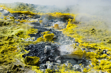 Yellow Sulphur on surface of rocks on top of a volcano crater on the island of Vulcano, Aeolian Archipelago. Sicily, Italy. Gray white and Yellow background of Sulfur. Steam and smoke from fumarole
