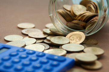 Gold coins on wooden desk with blurred calculator and jar. Business or finance concept.