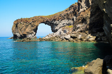 Natural volcanic arch formed from lava on the crystal clear tyrrhenian sea in Punta Perciato, Pollara, Salina. Rocky coastline, Aeolian Islands Archipelago, Sicily, Italy.
