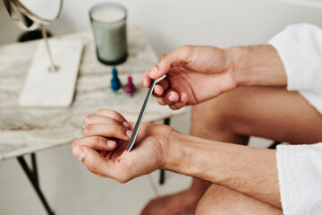 Close-up of man polishing his fingernails with file after bath procedure