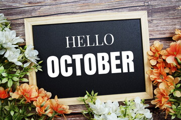 Hello October typography text written on wooden blackboard with flower bouquet decorate on wooden background