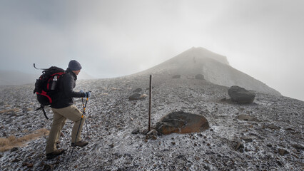 Hiking the steep scree terrain to the Red Crater summit with strong southerly wind on Tongariro...