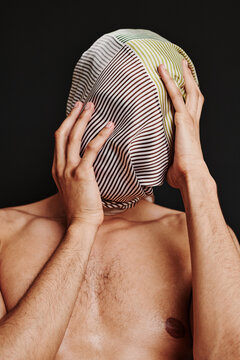 Portrait of shirtless young man trying to take headscarf off his head isolated on black background
