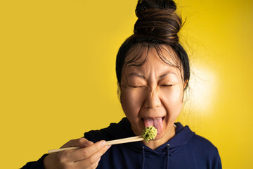 Funny young asian woman holding spicy wasabi show tongue