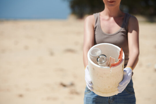 Cropped image of female vounteer showing bucket with glass bottles and plastic garbage she found on sandy beach