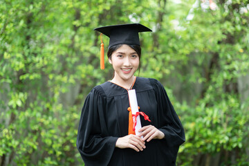 Attractive Asian Women Student Graduate in cap and gown celebrating with certificate in hand and so...