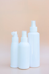 Set of three white spray bottles on beige background. Copy space, vetrical format
