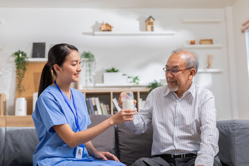Obraz premium Asian beautiful therapist doctor serve milk to older patient in nursing home. Asian nurse in blue uniform assist elderly senior man to drink milk in hand while sitting at couch.Elderly care concept