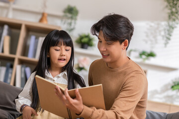 Happy asian young father smile reading fairy tale story with daughter in living room at home....