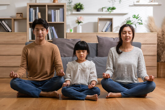 Calm asian family doing yoga meditation concentrate of deep breath at home.Peaceful young parent exercise breathing together for healthy mind.Father Mother and Little Daughter practice yoga meditate