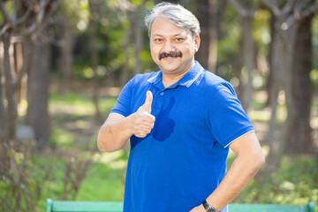 Portrait mature smiling indian senior man standing at park doing thumbs up gesture, Happy Elderly...