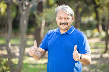 Portrait mature smiling indian senior man standing at park doing thumbs up gesture, Happy Elderly...