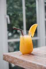 Glass of fresh orange juice and  straw on the wooden table in cafe house.