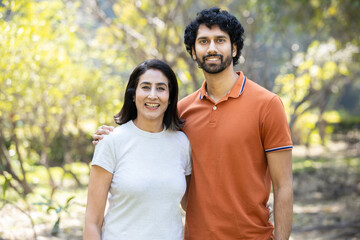 Fototapeta premium Portrait of happy indian couple standing outdoors in the park, Smiling urban city man and woman wearing casual t-shirt, looking at camera. husband wife.