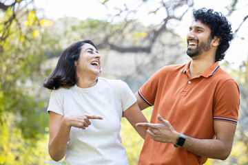 Happy indian couple laughing in the park, cheerful urban man and woman wearing casual t-shirt...