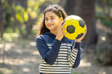 Portrait of young indian girl holding football in hand while standing at park outdoor, Asian female...