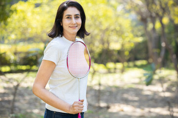 Portrait of mature urban indian woman holding badminton racket in the park. Smiling asian sporty...