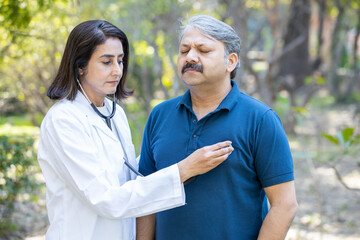Female indian doctor check heart beat of senior male patient stethoscope outdoor park, aging,...