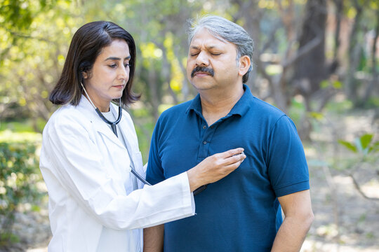 Mature Female Indian Doctor Wearing Apron Check Heat Beat Of Senior Male Patient With Stethoscope Outdoor In The Park, Healthcare, Illness.