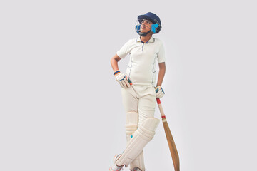 full length of a boy in cricket uniform standing with bat looking elsewhere
