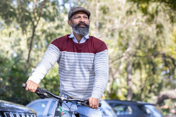 Fototapeta na wymiar Happy Indian mature beard man wearing cap ride bicycle outdoor in the park outdoor.