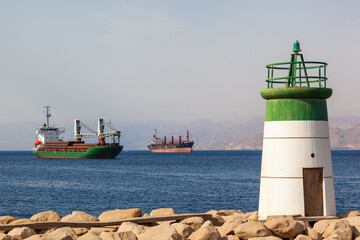 Small lighthouse on the coast of Aqaba, Jordan, with cargo ships in the background. Situated on the Red Sea, this is the only sea port in Jordan