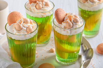Tasty green jelly with peaches, sprinkles and cream. - obrazy, fototapety, plakaty