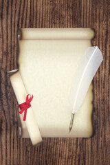 Parchment paper scroll with feather quill pen and rolled scroll on rustic wood background....