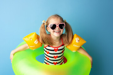 Funny happy child in bright swimsuit and sun glasses smiling and holding a swimming ring on colored...