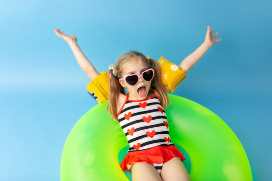 Happy little child girl in a swimwear suit lying on a bright inflatable circle and smiling. Blue background. Top view. Summer and vacation concept