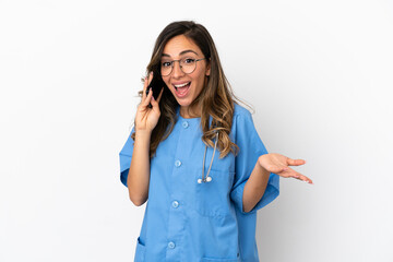 Young surgeon doctor woman over isolated white wall keeping a conversation with the mobile phone with someone