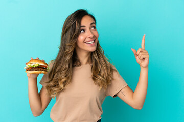 Young woman holding a burger over isolated background pointing up a great idea