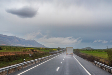 Truck circulating on the straight of a highway on a rainy day, raising a cloud of water as it passed.
