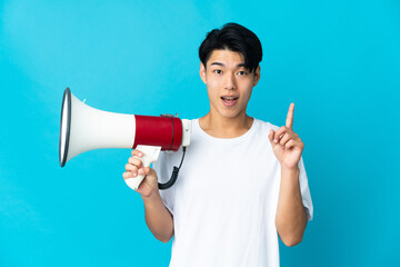 Young Chinese man isolated on blue background holding a megaphone and pointing up a great idea
