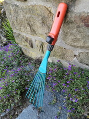 Handlicher kleiner Rechen für die Gartenarbeit im Frühling auf einer Terrasse mit Naturstein und...