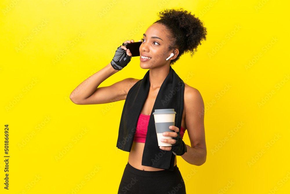 Canvas Prints Young African sport woman isolated on yellow background holding coffee to take away and a mobile